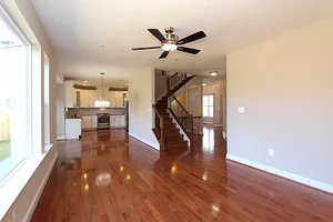 Open-concept living area with polished hardwood floors, modern ceiling fan, and renovated kitchen in the background, completed by Blue Horizon Renovations