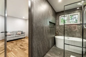 Modern bathroom remodel with large-format gray tile, freestanding tub, and adjacent finished living space completed by Blue Horizon Renovations.