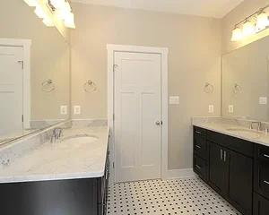 Bright modern bathroom remodel by Blue Horizon Renovations featuring dual vanities, marble countertops, large mirrors, and black-and-white tile flooring.