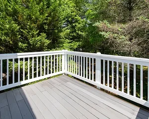Newly renovated gray deck with white railing surrounded by lush green trees, completed by Blue Horizon Renovations.