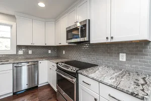 Modern kitchen remodel with white shaker cabinets, stainless steel appliances, gray subway tile backsplash, and marble-style countertops by Blue Horizon Renovations.