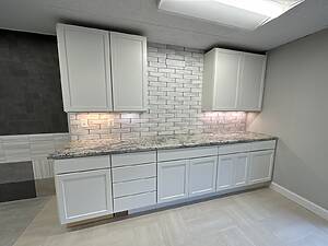 Modern white cabinetry with granite countertop and subway tile backsplash installed in a remodeled space by Blue Horizon Renovations.