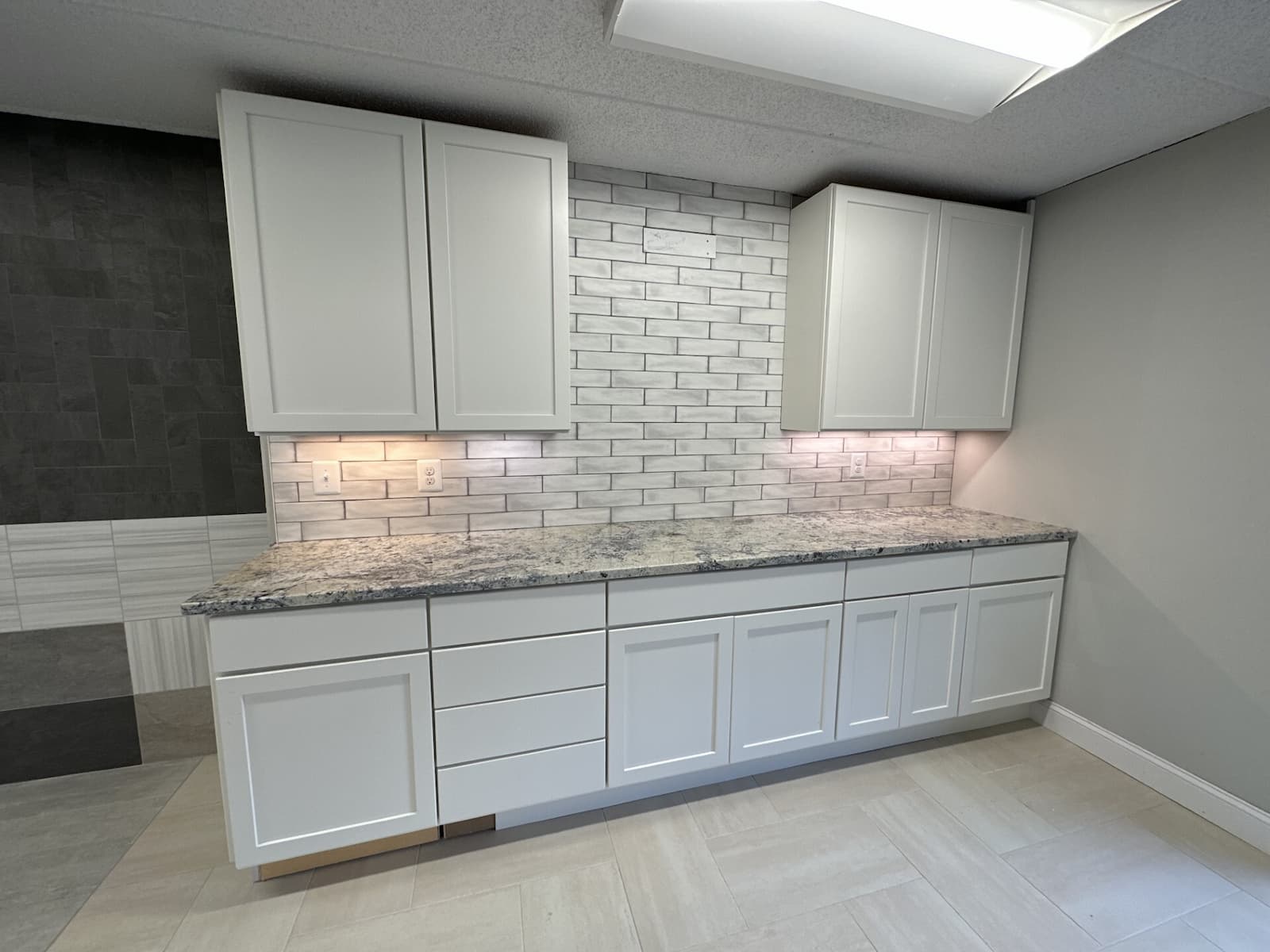 Modern kitchen design trend featuring white shaker cabinets, gray and white granite countertop, and a white subway tile backsplash with under-cabinet lighting.