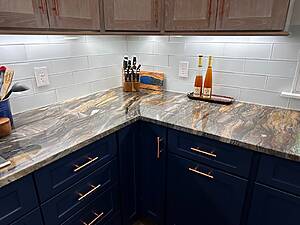 Kitchen design featuring multi-colored granite countertops with blue base cabinets, wood upper cabinets, copper hardware, and a light blue glass subway tile backsplash.