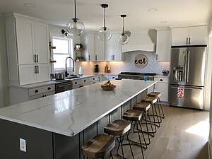 Modern farmhouse kitchen remodel with a large marble island, white shaker cabinets, pendant lighting, and stainless steel appliances completed by Blue Horizon Renovations.
